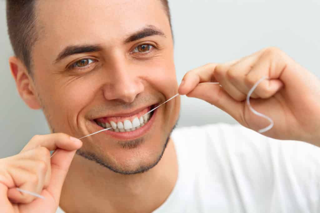Closeup of young man flossing his teeth. Cleaning teeth with dental floss