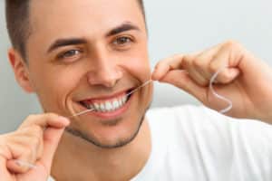 Closeup of young man flossing his teeth. Cleaning teeth with dental floss