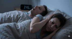 A man snoring while he sleeps. His partner is covering her ears while trying to get back to sleep.